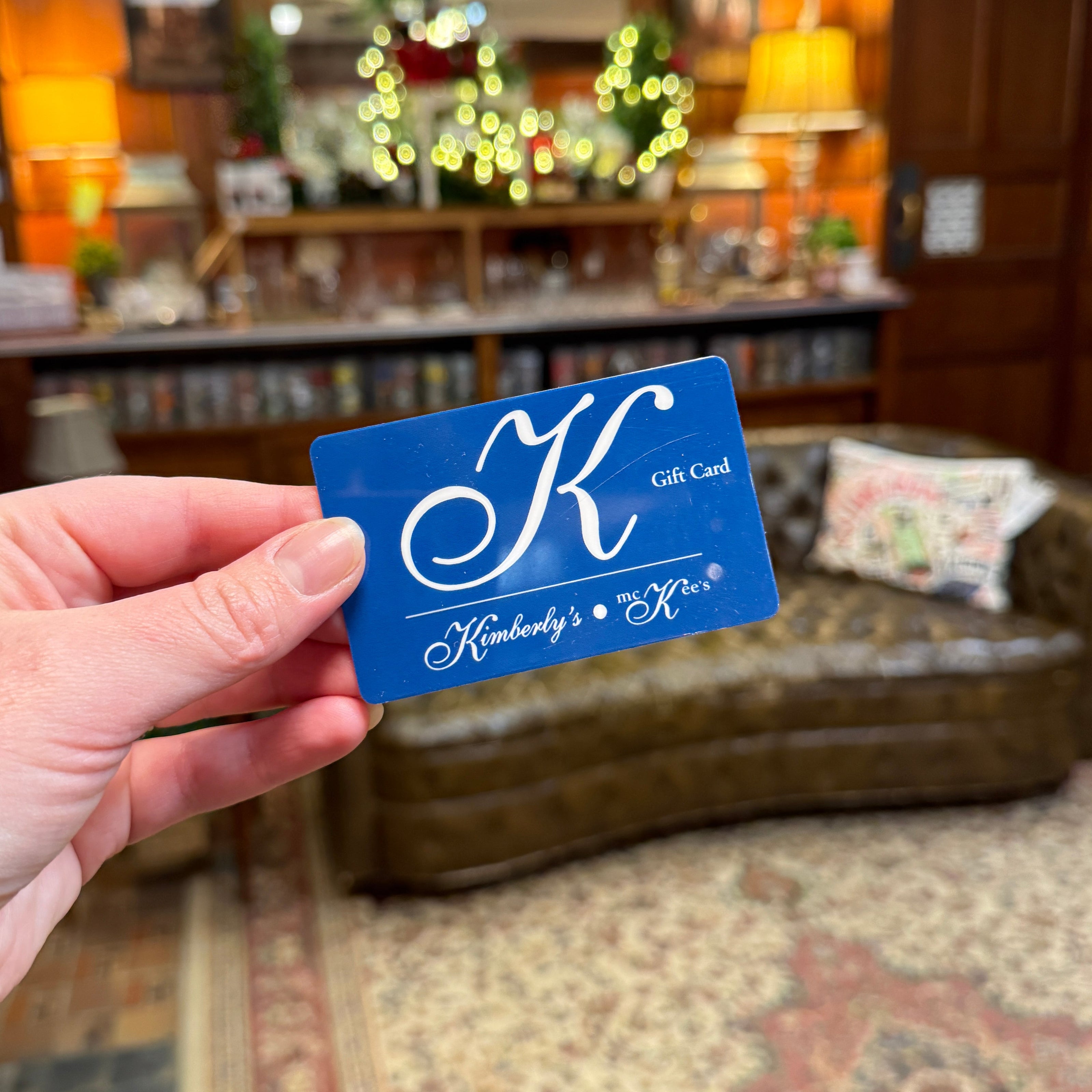 Hand holding a blue gift card with a decorative design in an indoor setting