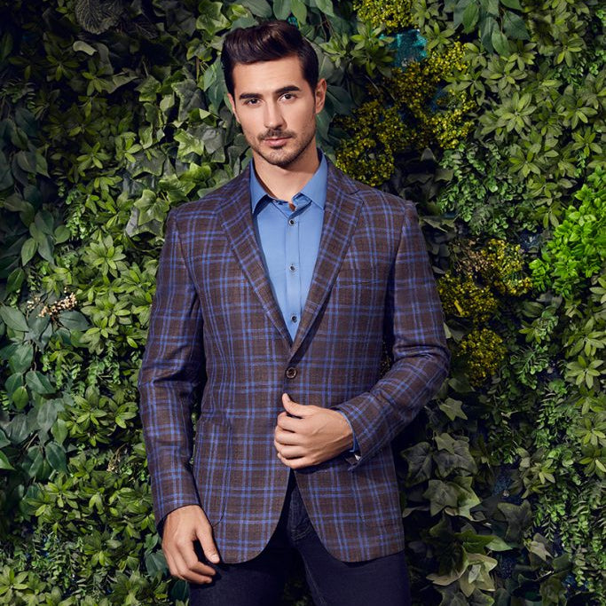 Man wearing a plaid blazer and blue shirt against a green leafy background