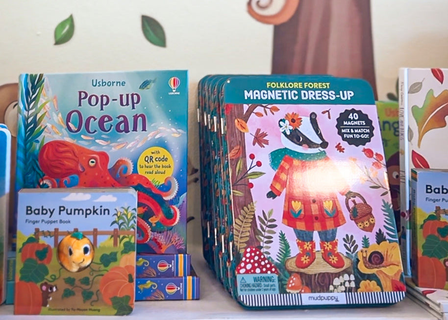 Children's books on a shelf with a tree and animal decorations in the background