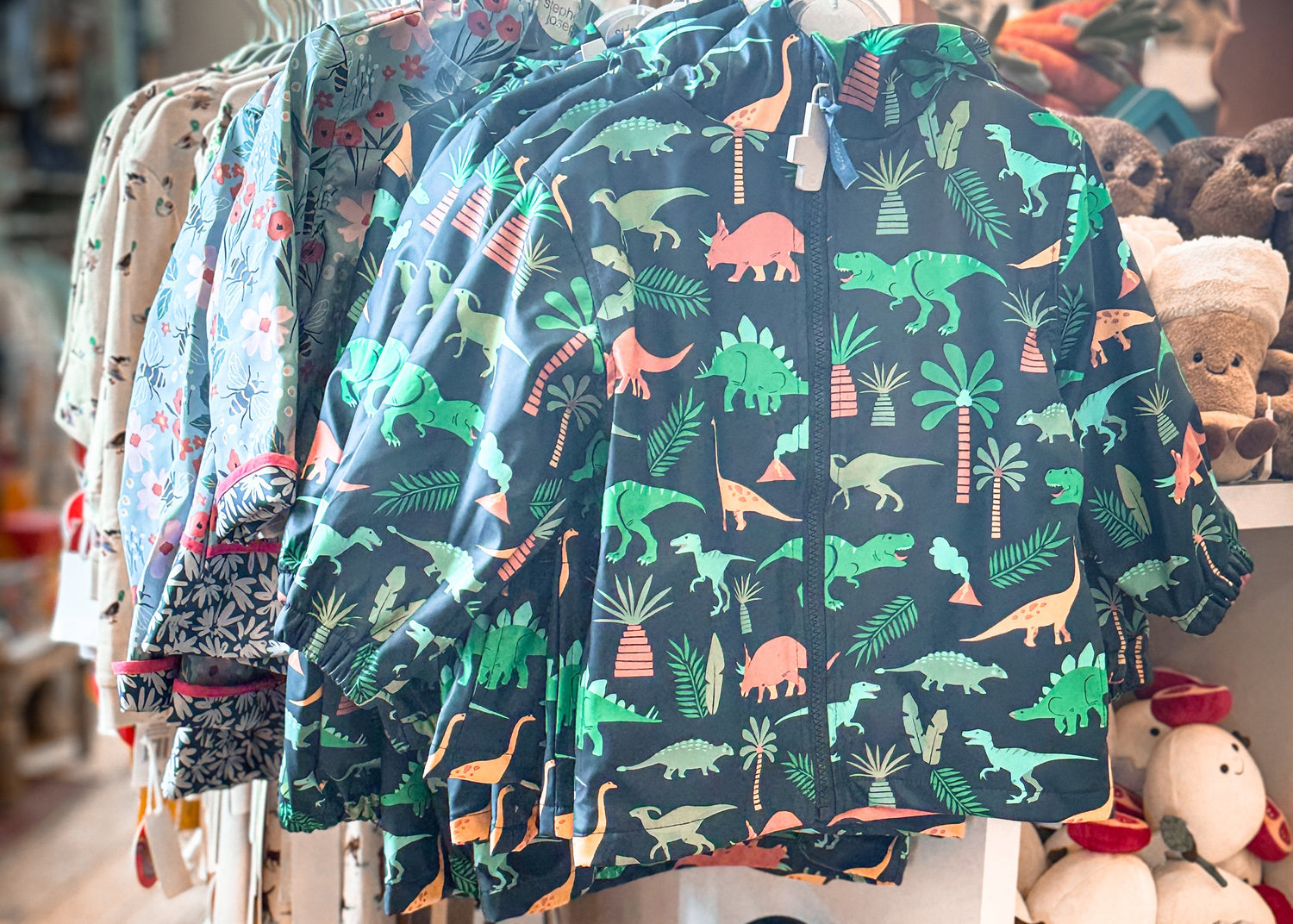 Children's clothing with dinosaur pattern on hangers in a store setting.