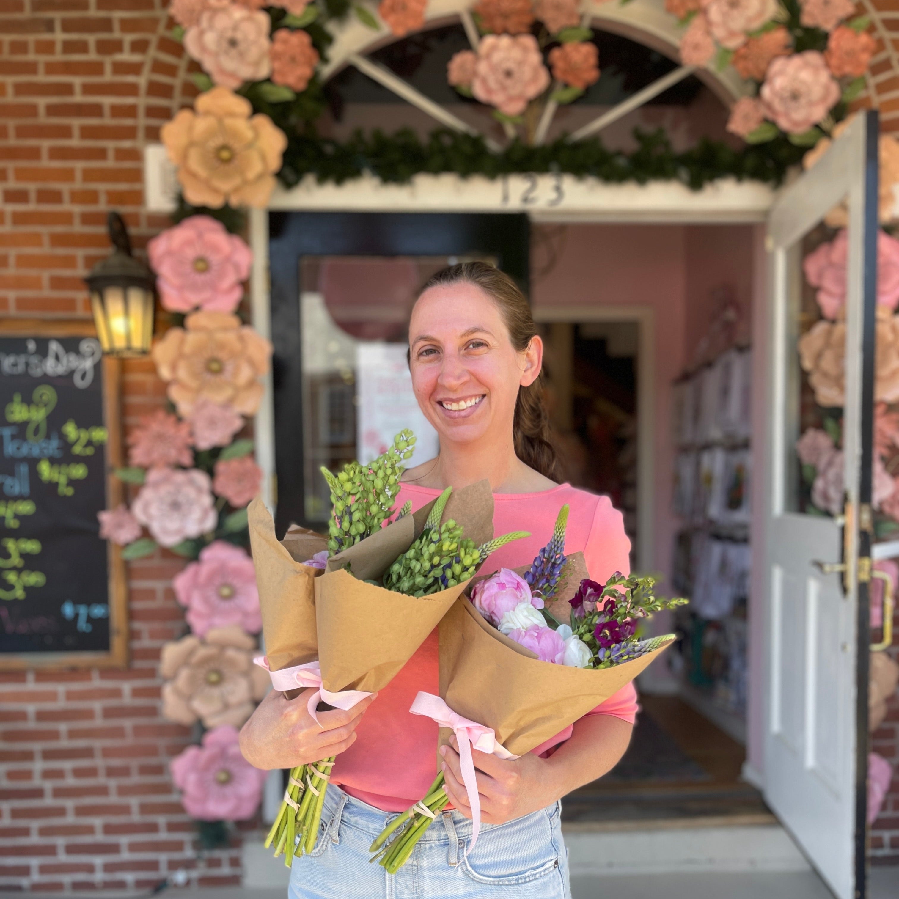 A woman holding three bouquets and smiling stands outside The Market at Kimberly's at the Mother's Day Bloom Bar Event.